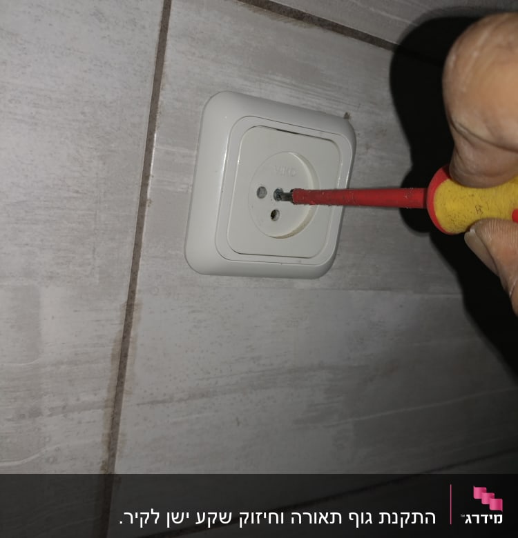 מברג ביד חשמלאי מתקן שקע חשמל בקיר
